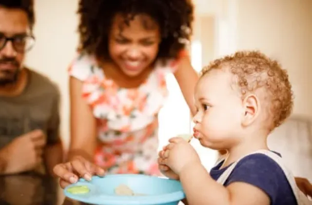 Mom and dad watching baby eat healthy food