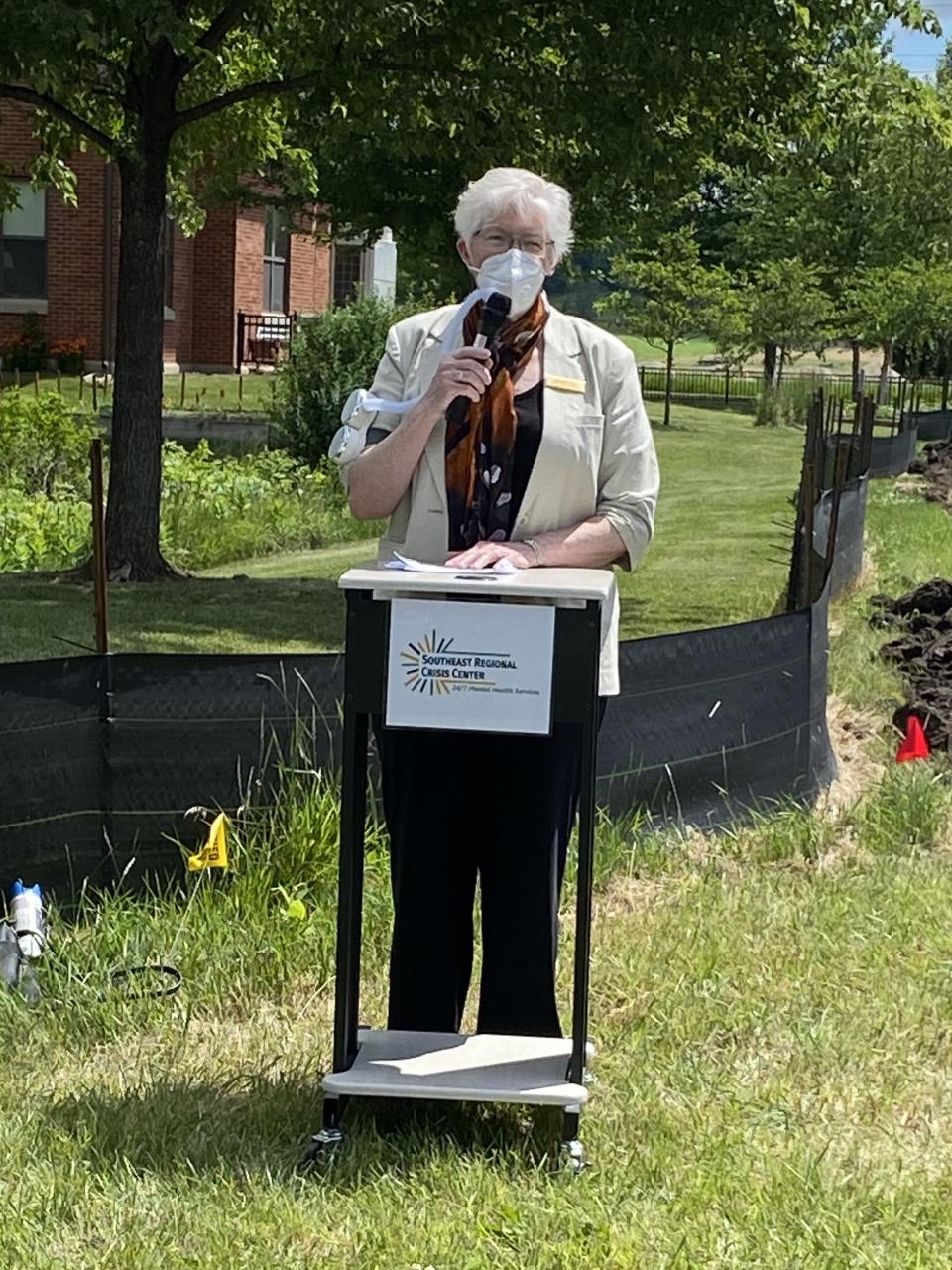 Commissioner Podulke standing in front of a podium speaking into a microphone at SERCC groundbreaking