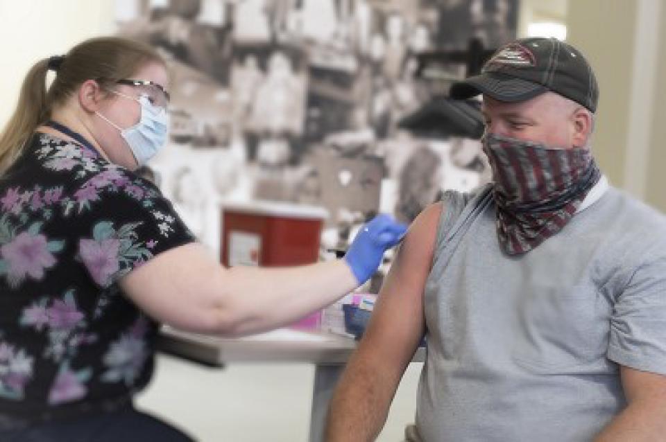 An EMT worker wearing a mask receiving his COVID vaccine in his right arm from a registered nurse