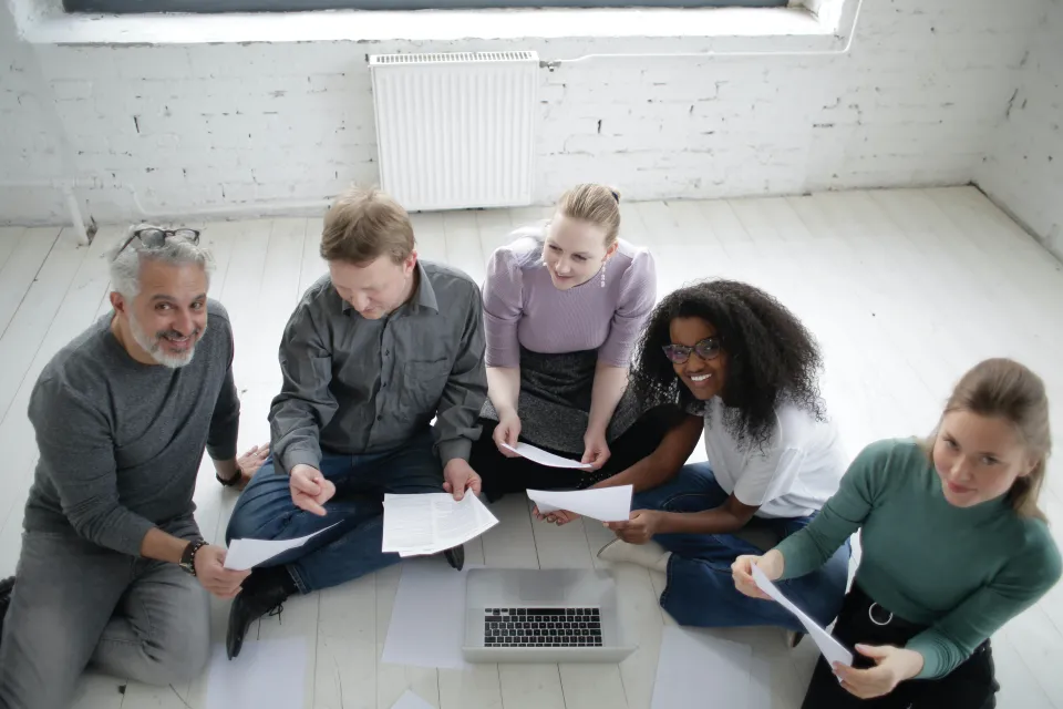 Five people sitting in a work place around a laptop
