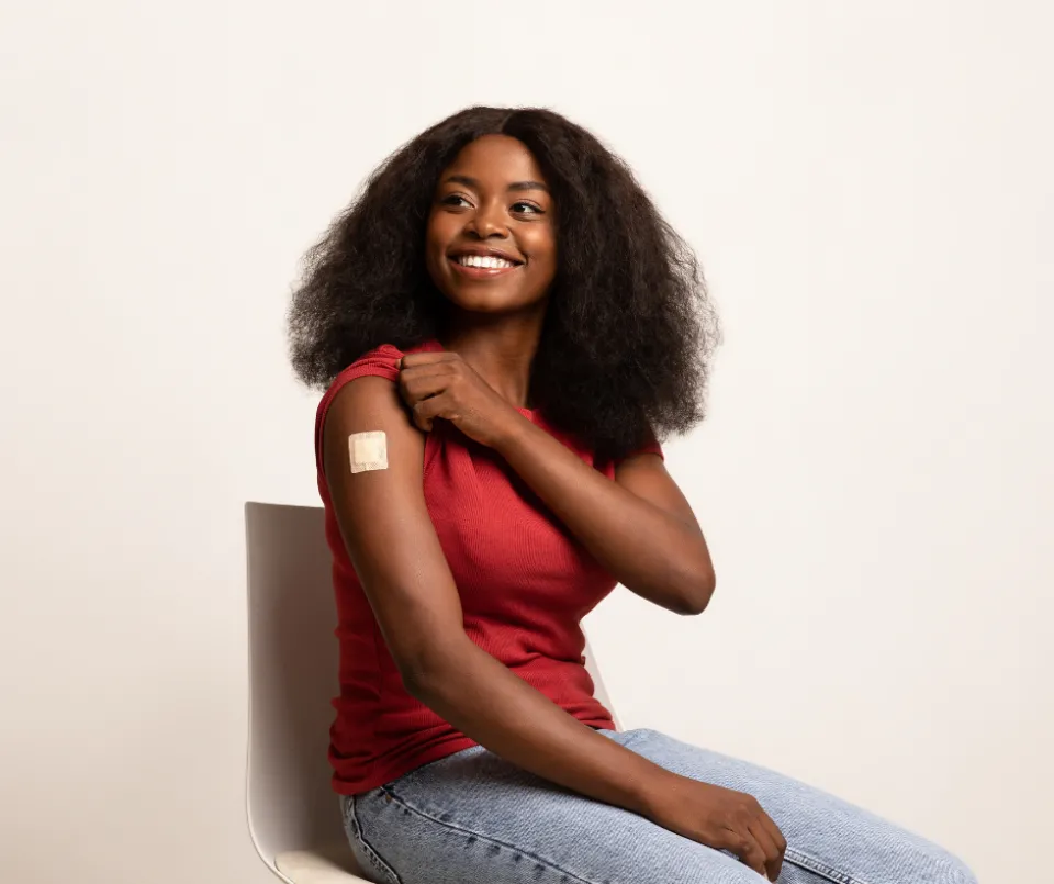 A person sitting on a chair. The person's t-shirt sleeve is rolled up, and a band-aid is on their arm.
