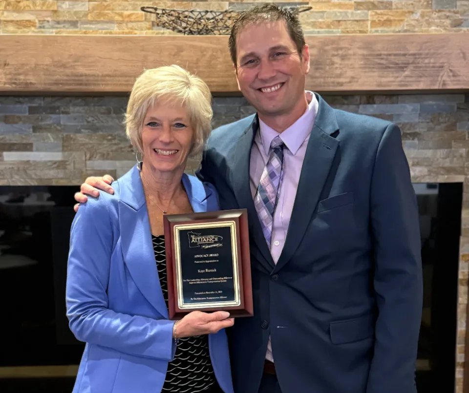 Kaye Bieniek and Ben Johnson posing for a photo while holding an award.
