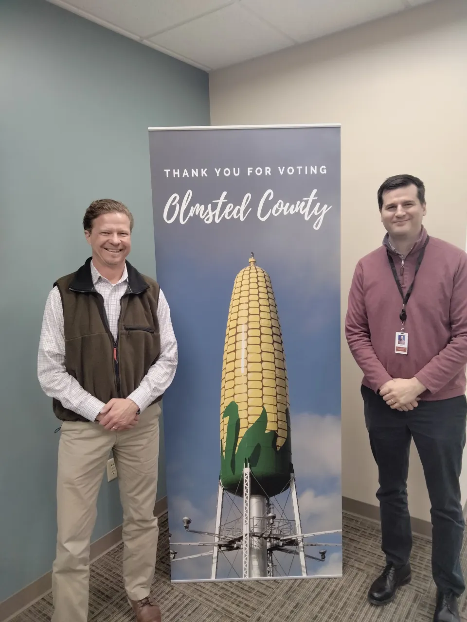Navigator team member and Luke Turner standing in front of Thank you for Visiting Olmsted County sign with corn tower