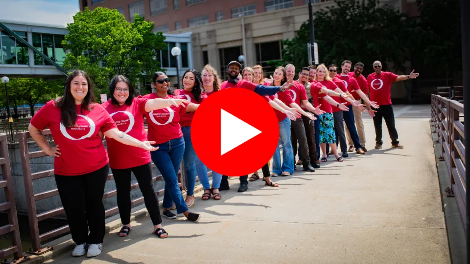 Olmsted County employees in matching shirts on bridge with YouTube play button overlaid
