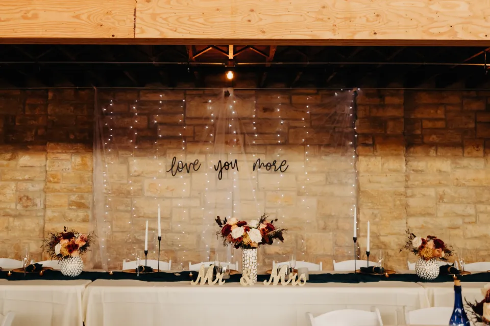 Wedding head table with decor and twinkle lights behind with a sign that reads love you more