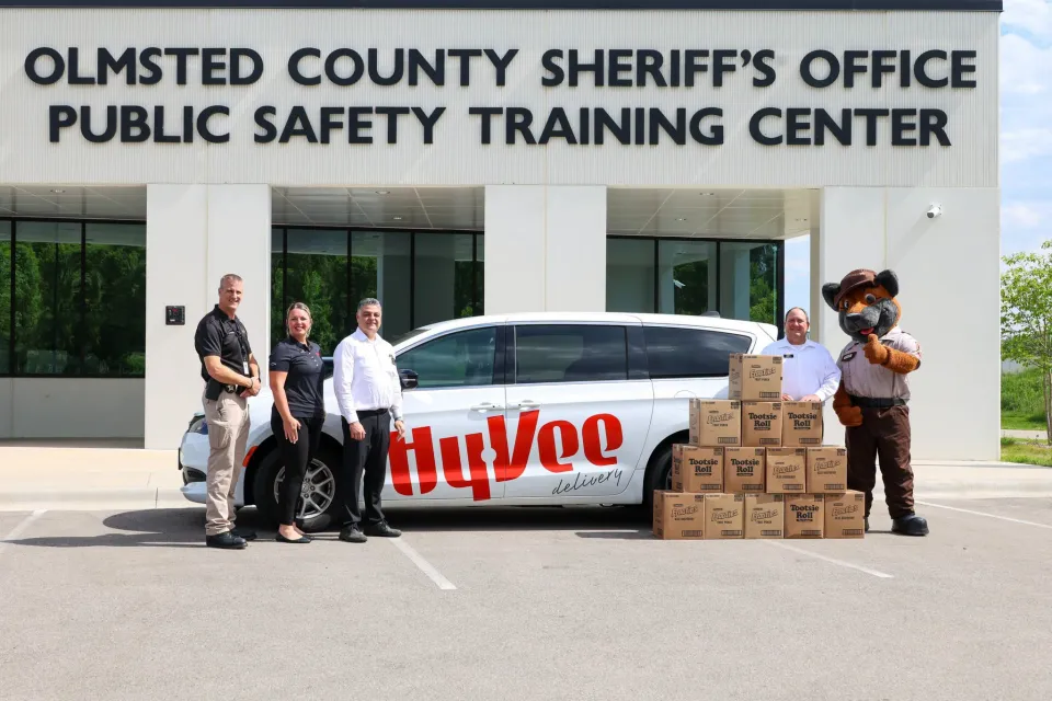 Members of the Rochester Hy-Vee team stand with Olmsted County Sheriff's Office staff in front of the Public Safety Training Center with donated candy and a Hy-Vee van.