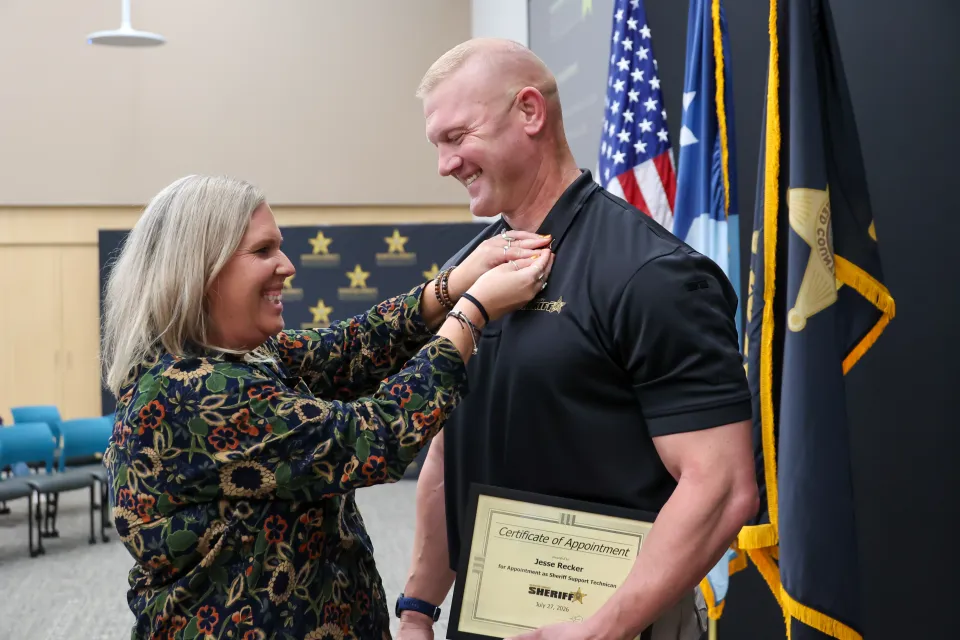 A member of the Olmsted County Sheriff's Office has a family member pin a badge to their polo after being publicly sworn in. 