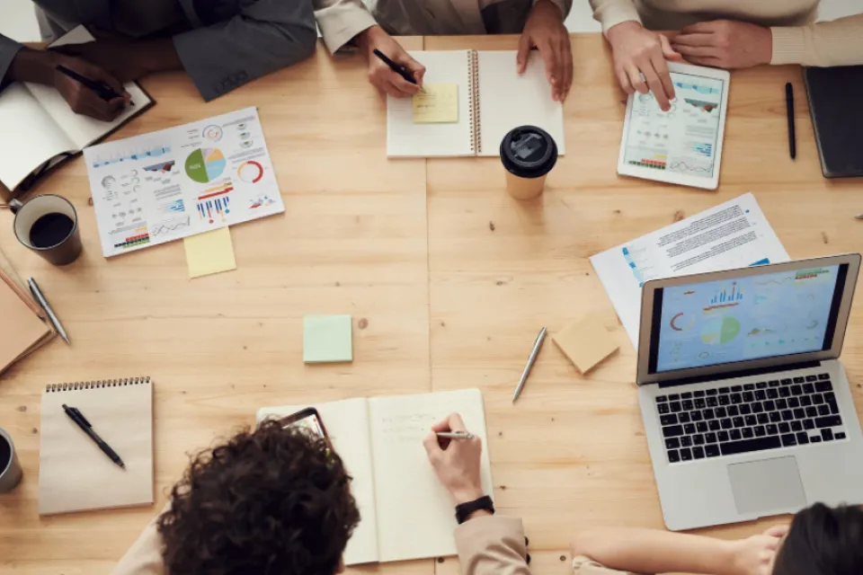 a Desk with paperwork, computer and people working together