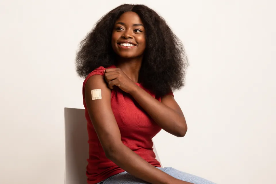 A person sitting on a chair. The person's t-shirt sleeve is rolled up, and a band-aid is on their arm.
