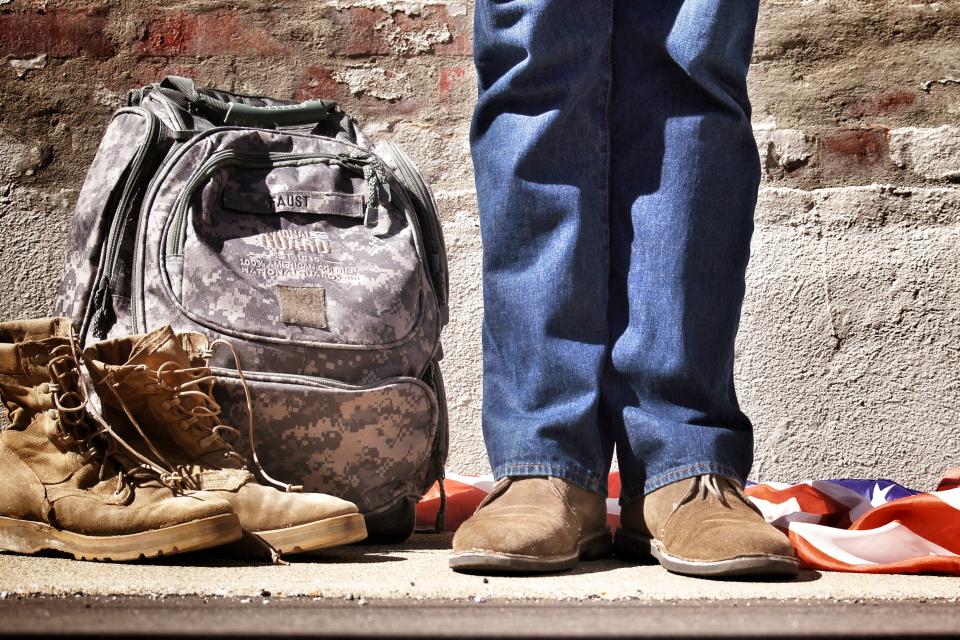 a veteran standing in front of the American flag and next to a backpack