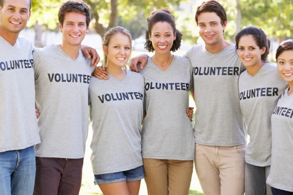A group of people standing in a line. Each shirt they are wearing says, "VOLUNTEER."