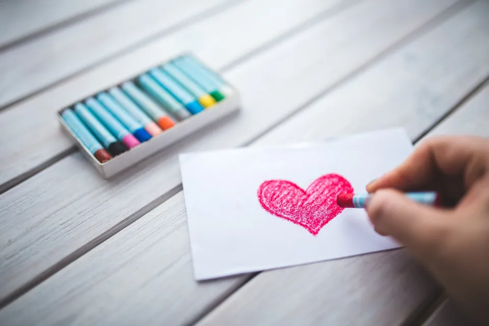 hand coloring a heart with crayons in the background
