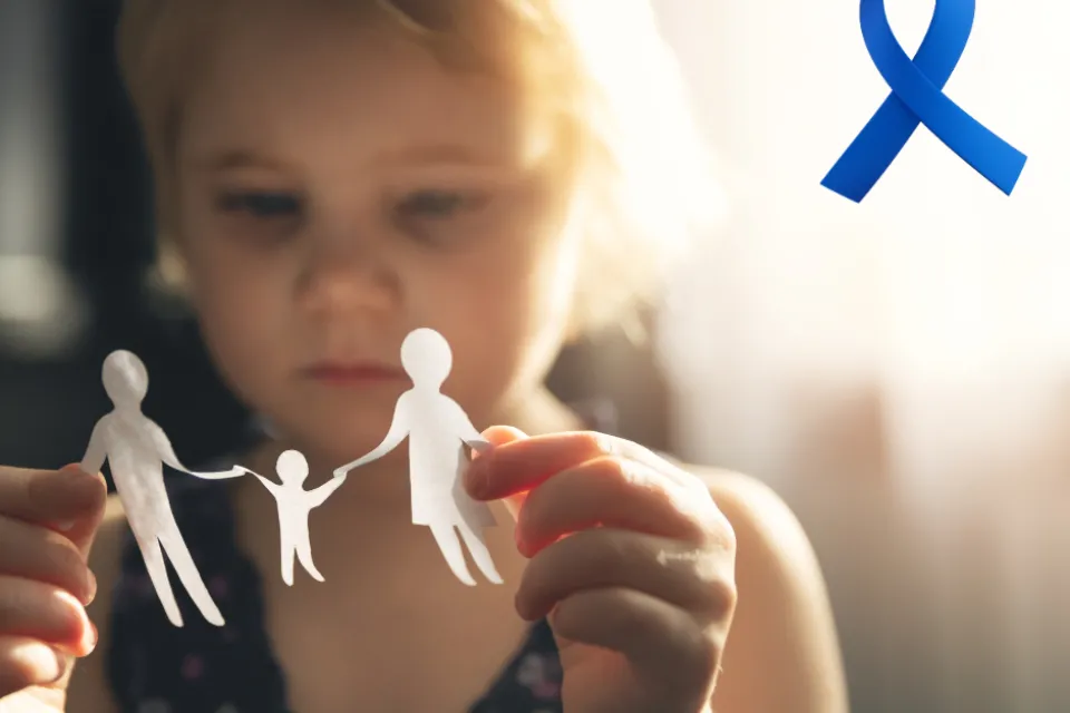 A child holding a paper cutout of a family. A blue ribbon in the upper right corner of the picture.