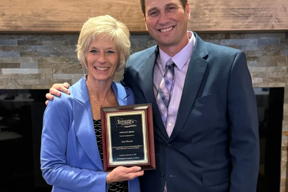 Kaye Bieniek and Ben Johnson posing for a photo while holding an award.