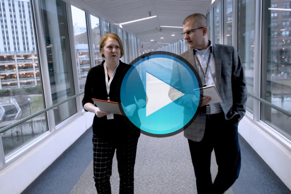 Travis Gransee walking down the skyway with a colleague. This thumbnail features a "play" button.