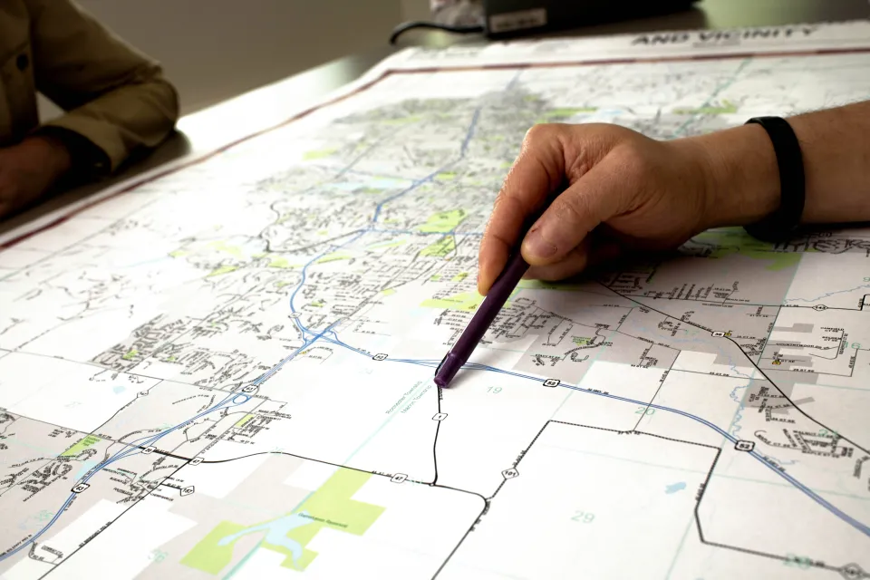 Person with pen in hand pointing at a road on a map.