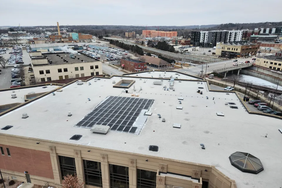 Aerial view of the Olmsted County Government Center rooftop covered in snow, featuring solar panels, with a background of a suburban landscape and construction cranes.