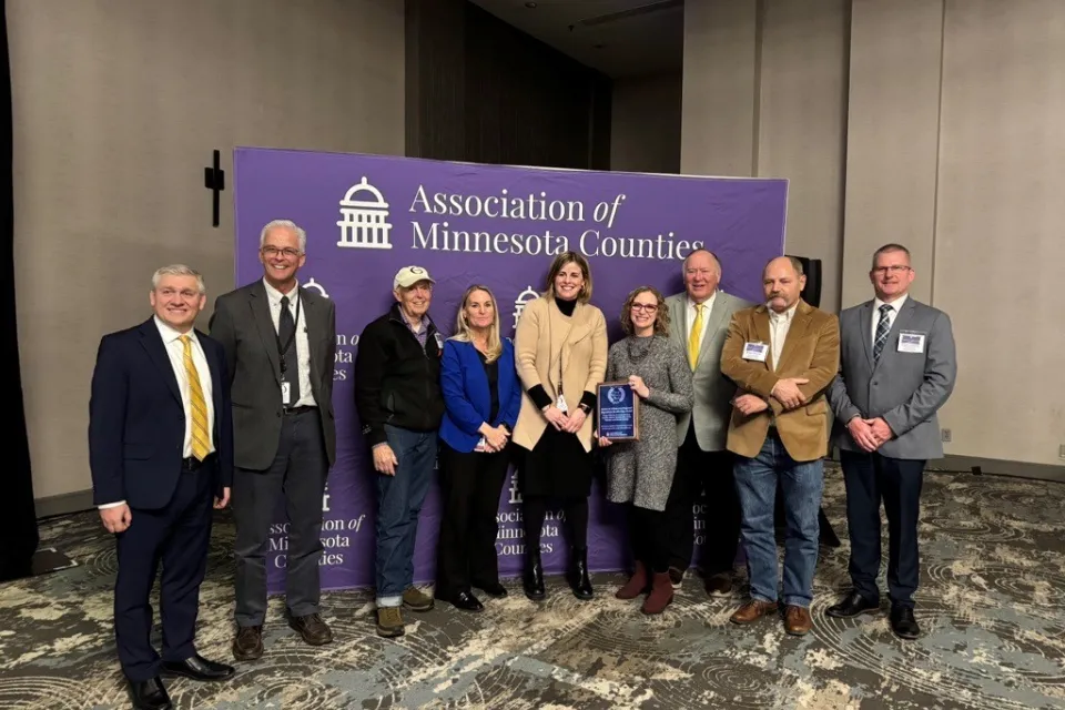 a group of people in front of an Association of Minnesota Counties banner with one person holding an award
