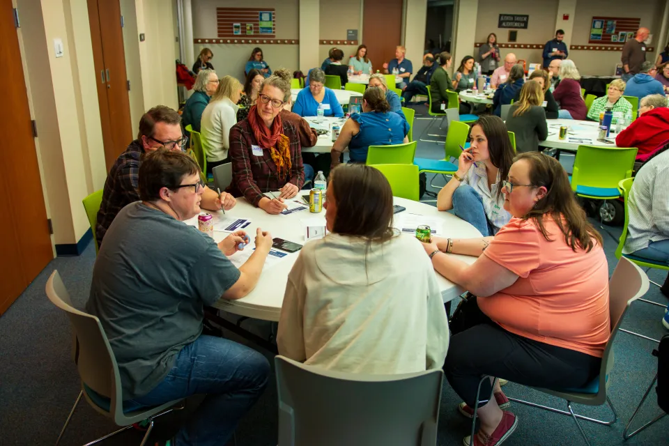 Group of people sitting around a table. Other people are sitting around tables in the background.